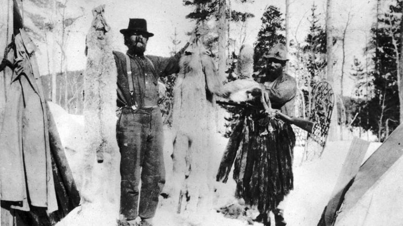 Two trappers showing off furs in a snowy forest.