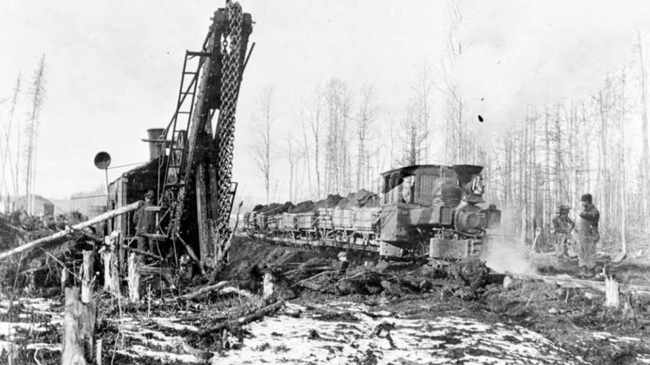 Steam-powered machinery clearing snow in a snowy forest.