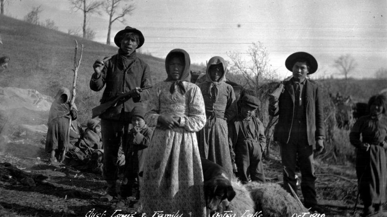 People standing outdoors on a hillside, dressed in early 20th-century rural attire.