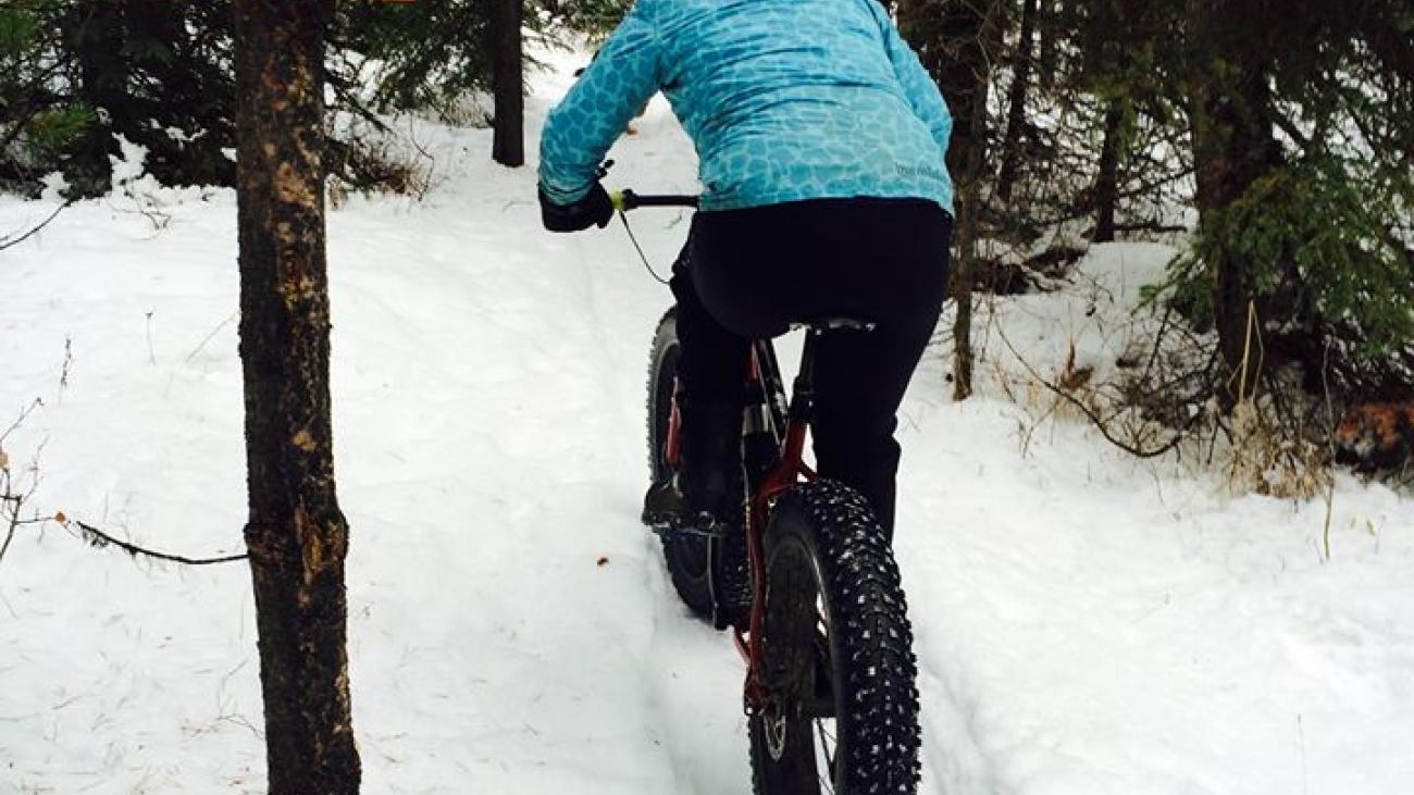 Cyclist on a snowy trail in the forest, wearing a blue jacket.