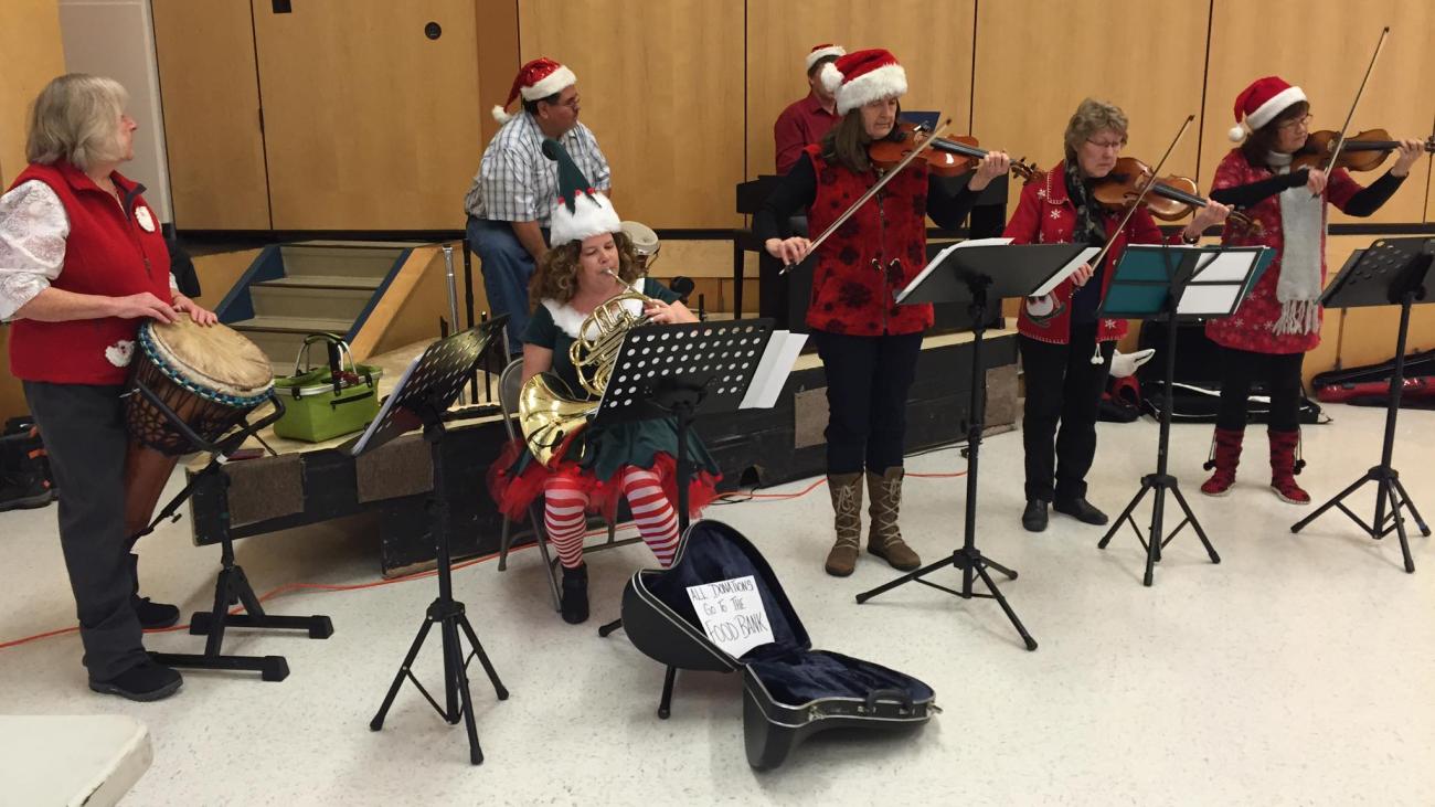 A group of musicians play music while wearing festive Santa hats indoors.