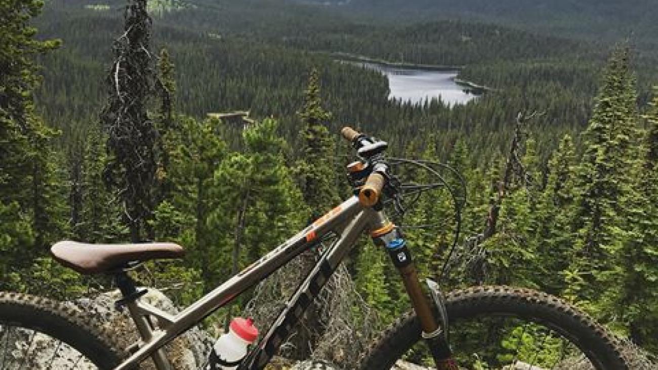 Mountain bike resting on a rocky trail overlooking a forested valley with a lake in the distance.