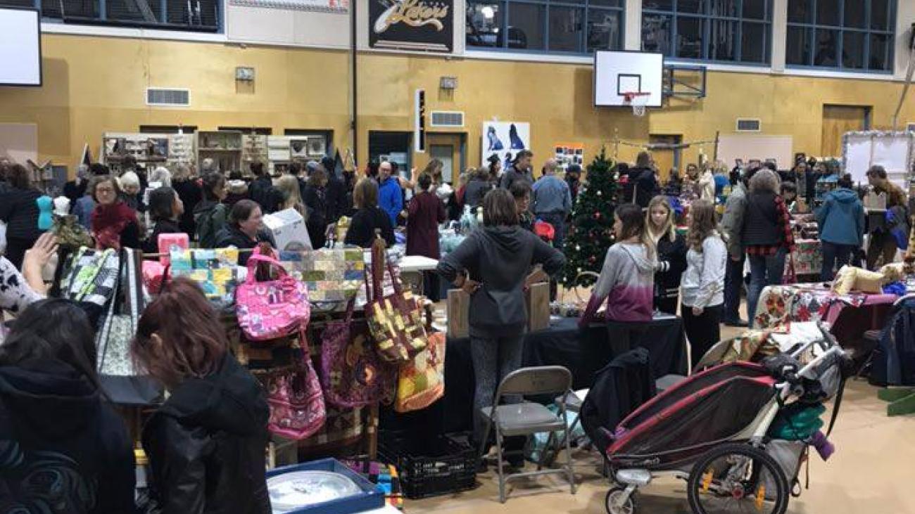 Crowded indoor market in a gymnasium with people browsing stalls.