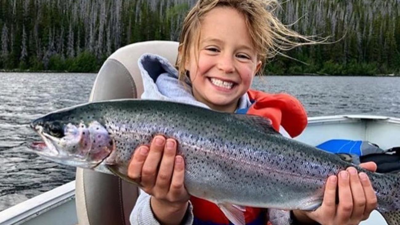 Young child smiling, holding a large fish on a boat.