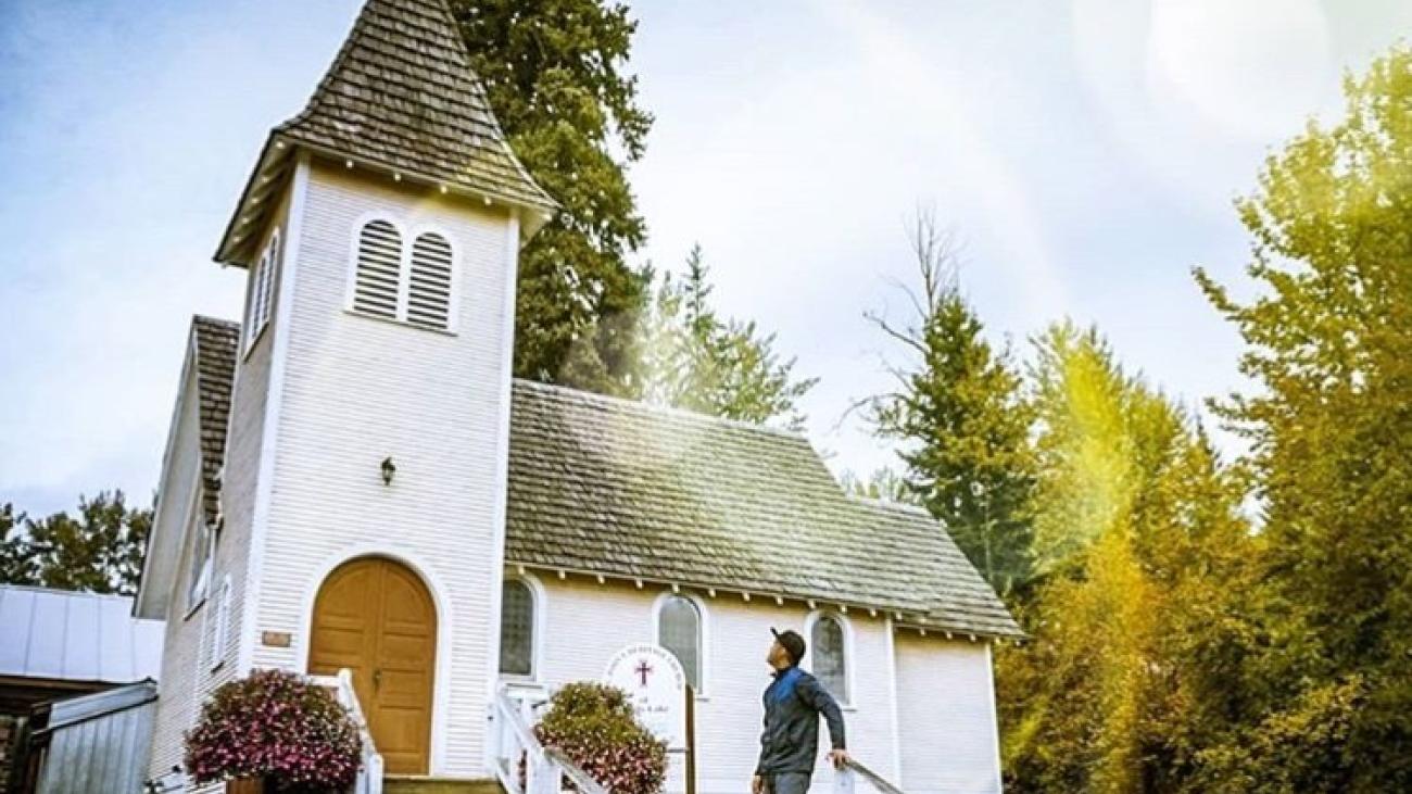 White church with steeple, surrounded by trees. There is a person standing outside.