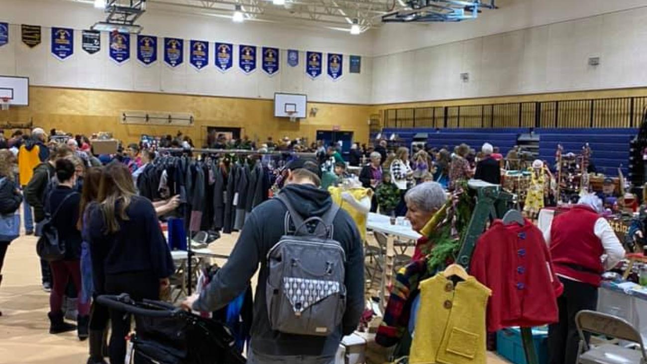 Busy indoor market with people browsing booths and tables in a gymnasium.