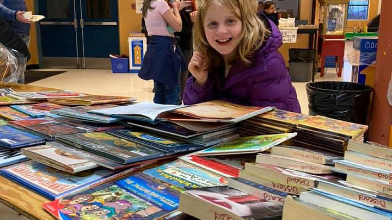 Child smiling at a table with colourful books.