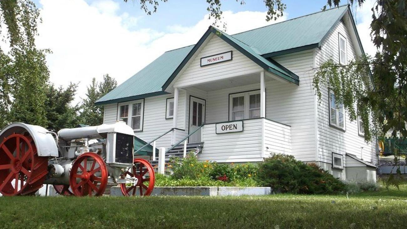 Small heritage museum with green roof and vintage tractor on display in front yard.