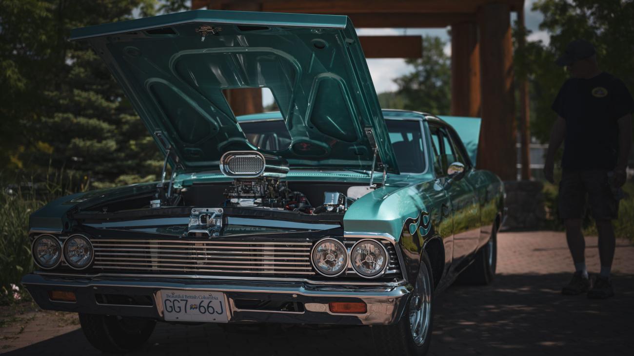 Turquoise classic car with hood open, parked outdoors in the shade.