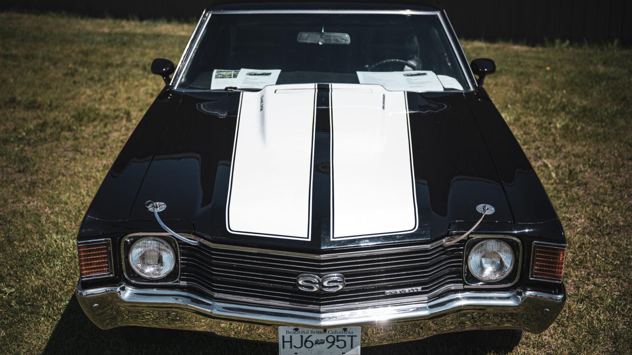 Classic black car with white racing stripes, parked on grass.