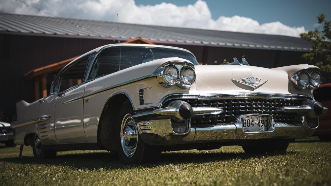 Classic white Cadillac parked on grass under a cloudy sky.