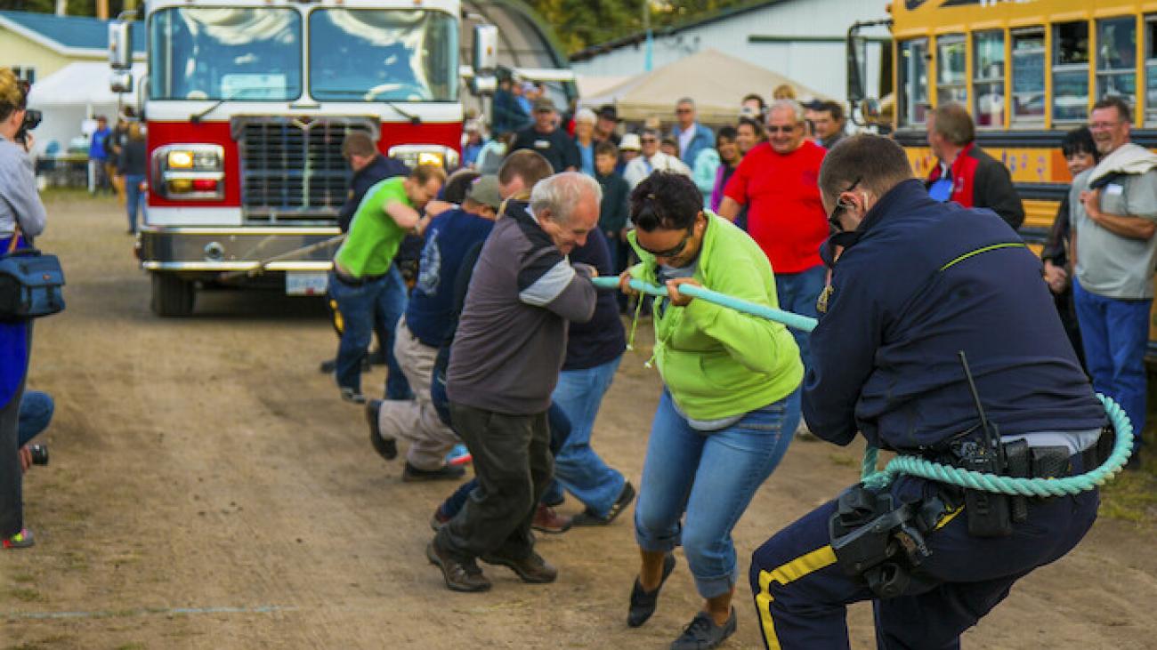Tug-of-war game between people and a fire truck in a rural setting.