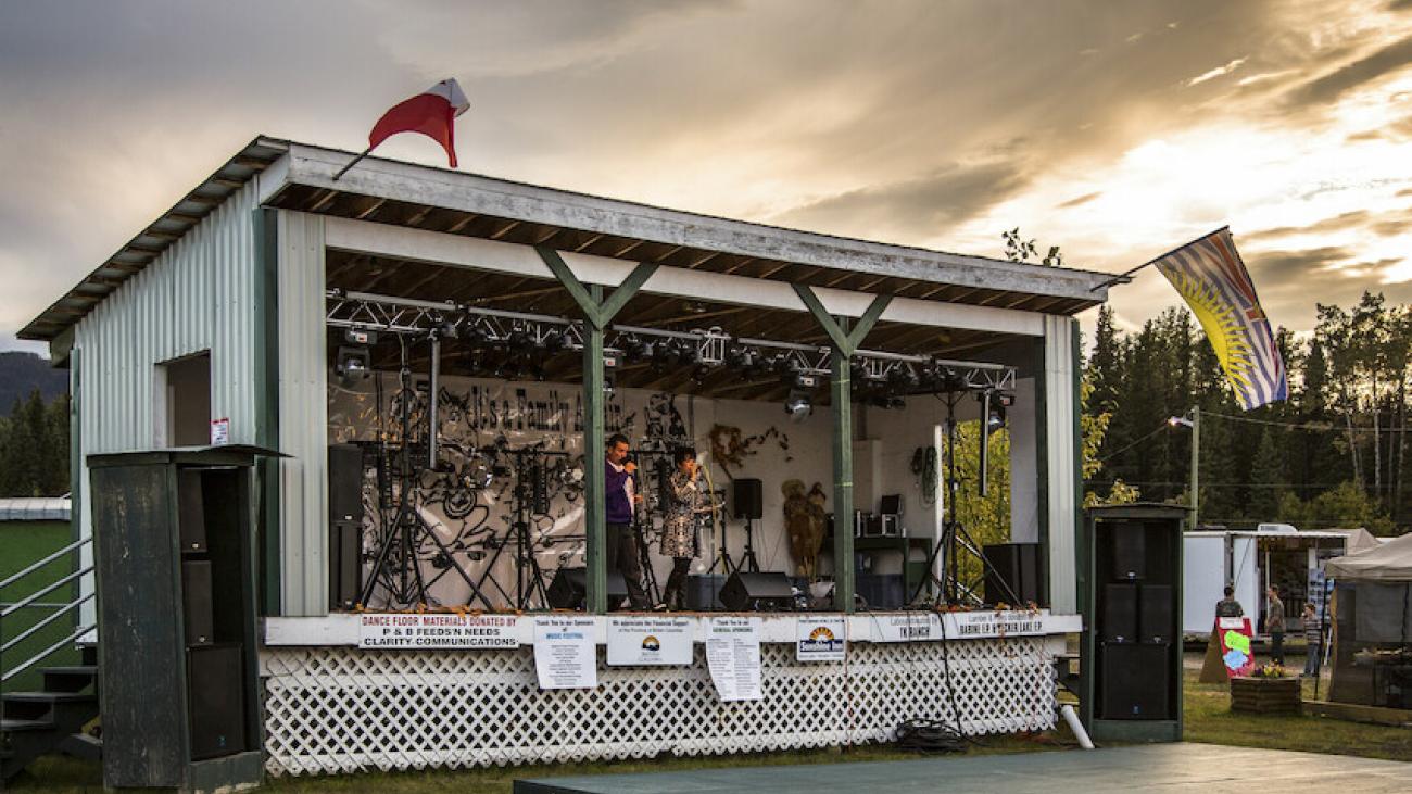 Outdoor stage with musical instruments, a red flag, and an American flag at sunset.