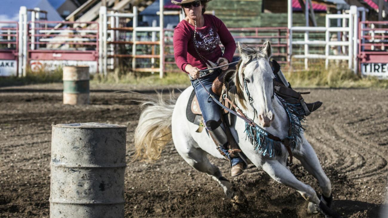 Cowgirl barrel racing a white horse in a rodeo arena.