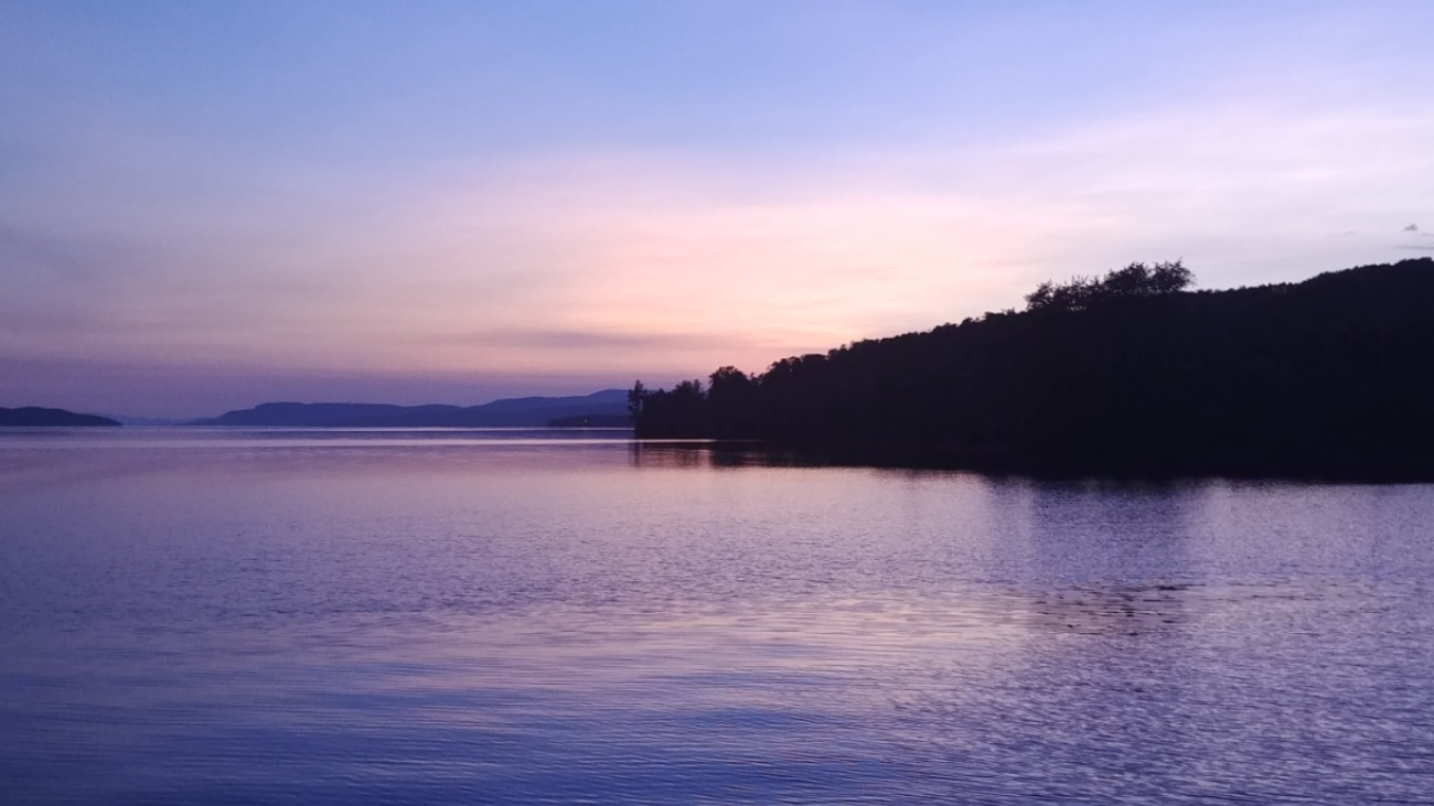 Twilight over a calm lake with a dark treeline silhouette.