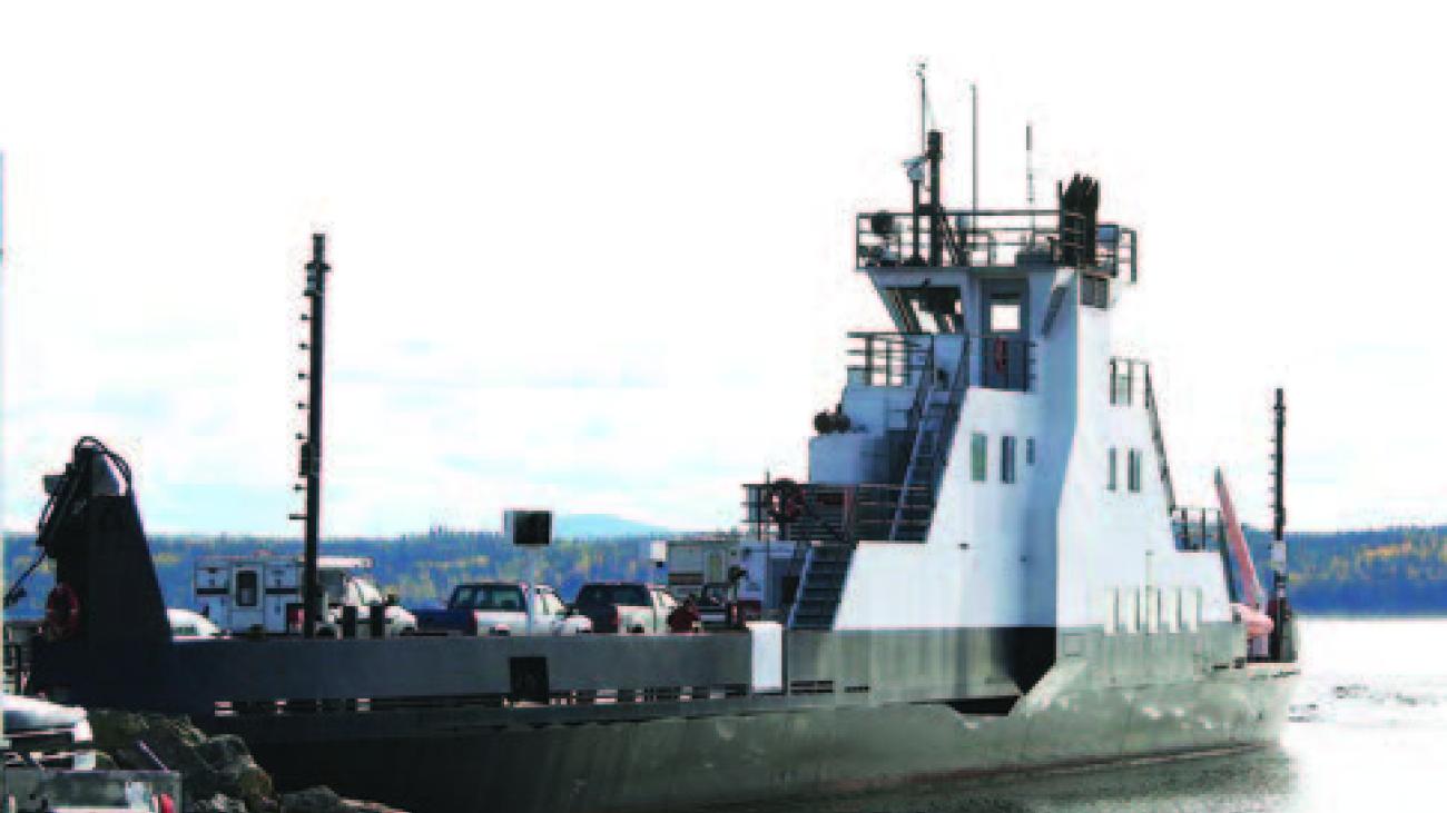 Ferry docked by rocky shore on a calm, cloudy day.