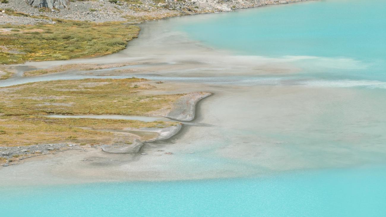 Two people walk by a bright turquoise lake in a rocky landscape.