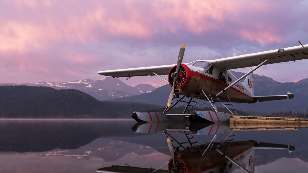 Seaplane on calm lake with pink sunset background.