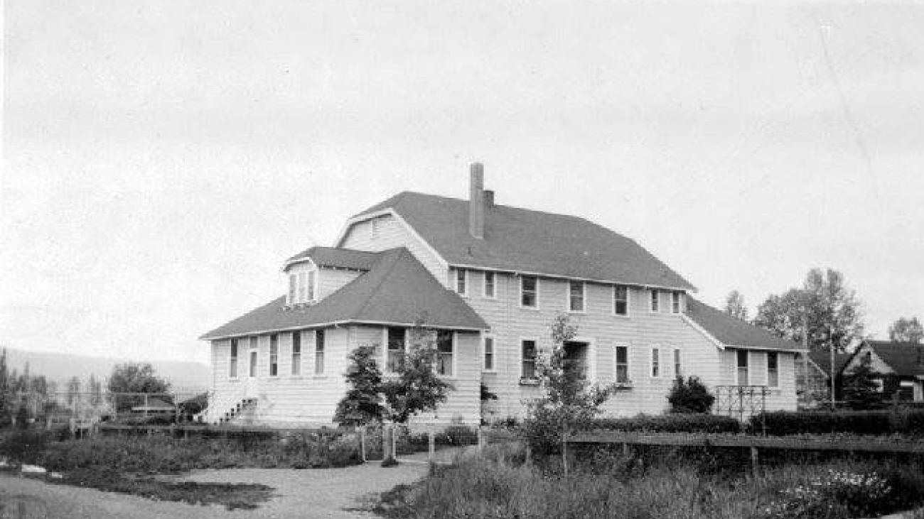 Large white house with multiple eaves and chimneys, surrounded by trees and grass.